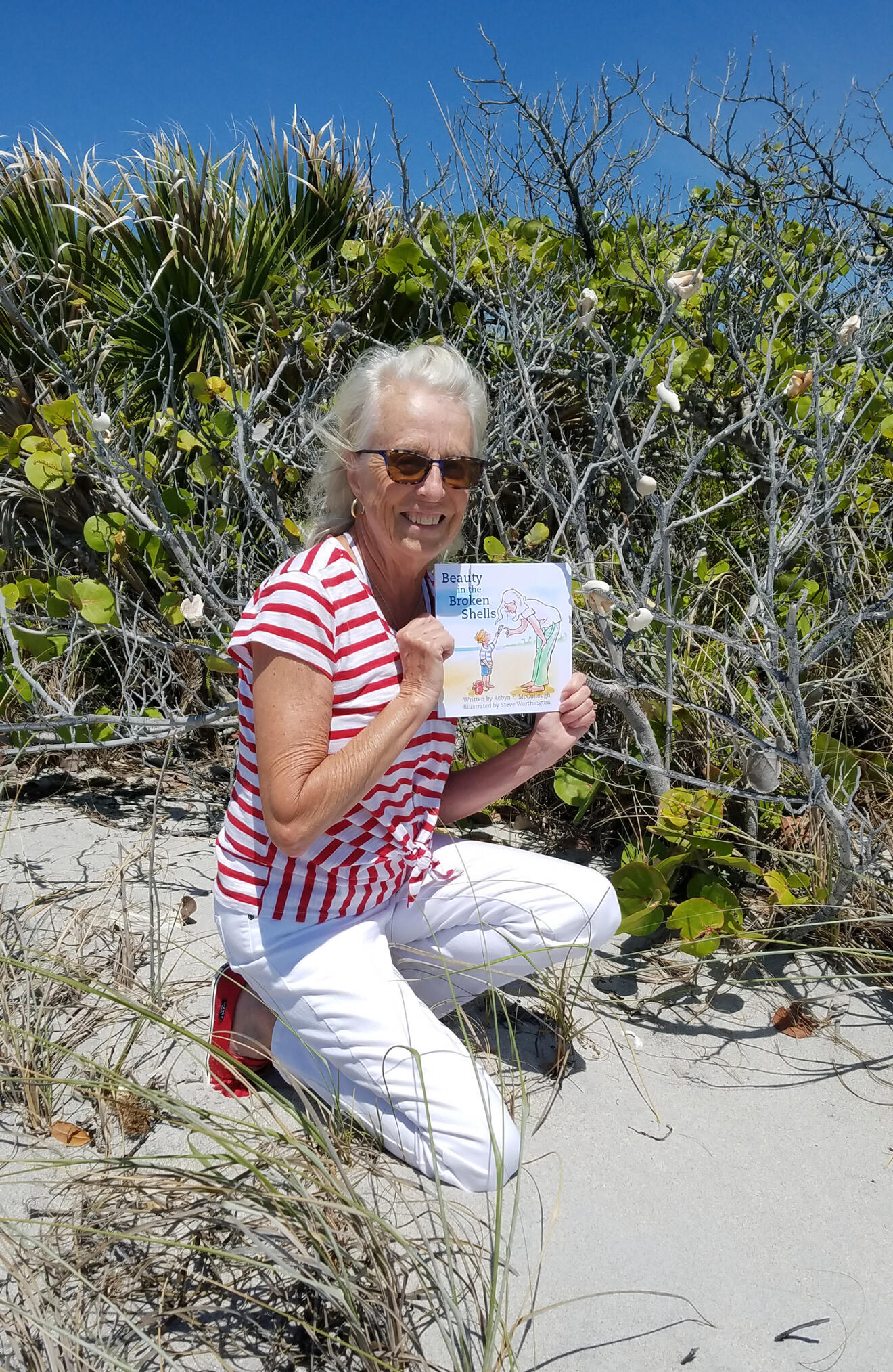 photograph of author Robyn McCullough on the beach holding a copy of her book "Beauty in the Broken Shells"